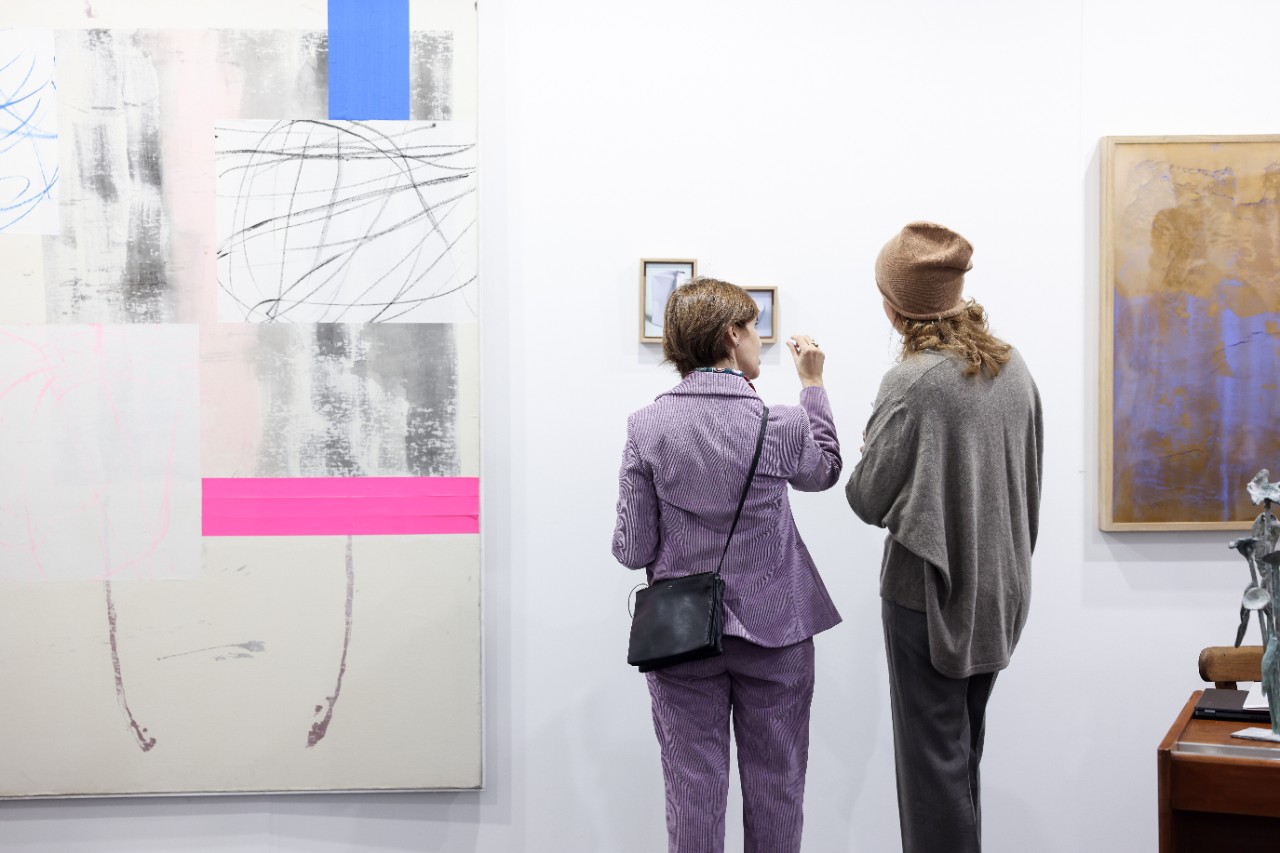 Besucher diskutieren über ein Gemälde am Stand einer Galerie.