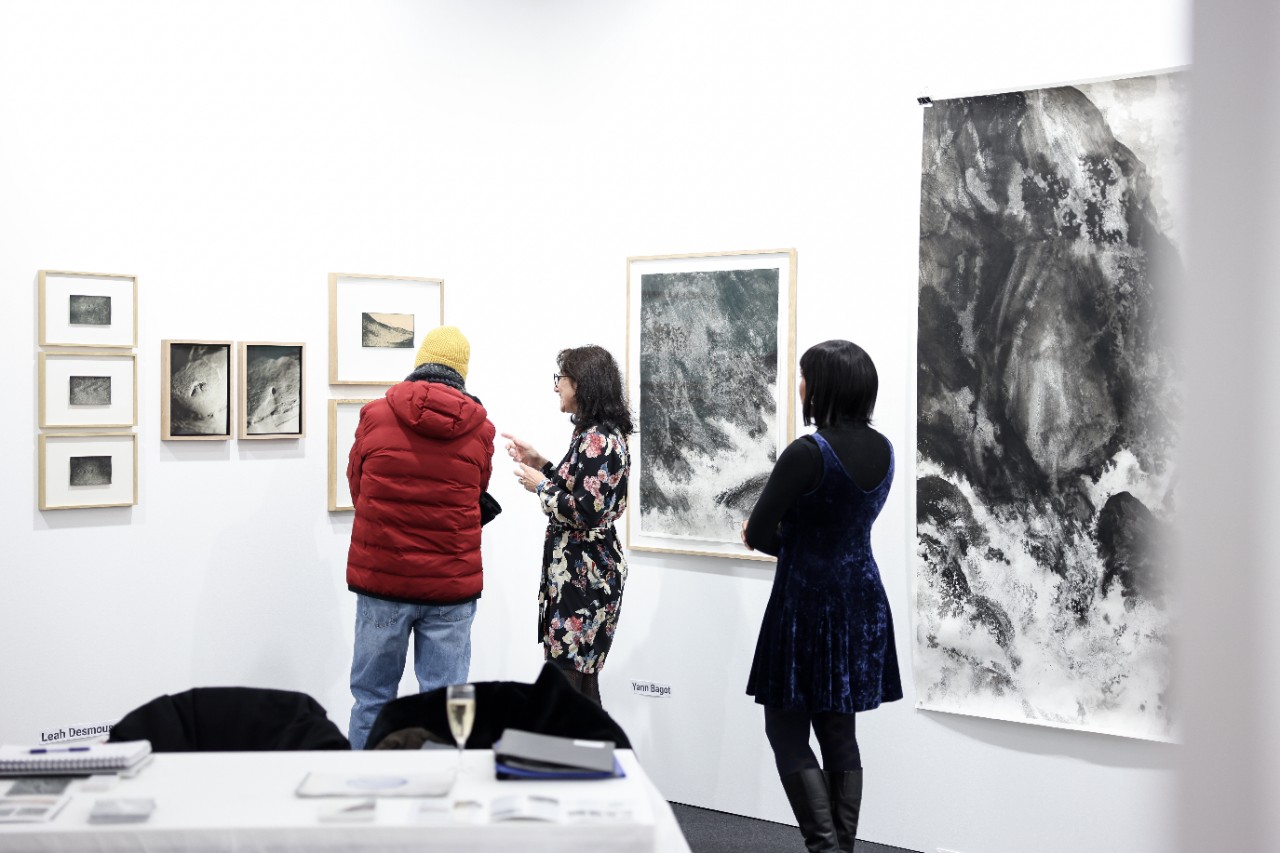 Visitors discussing a painting at a gallery's stand.