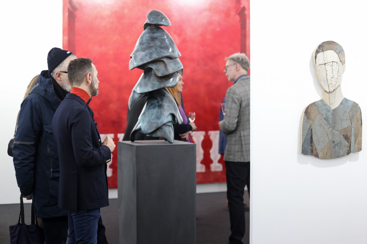 Visitors contemplating a sculpture at a gallery's stand.