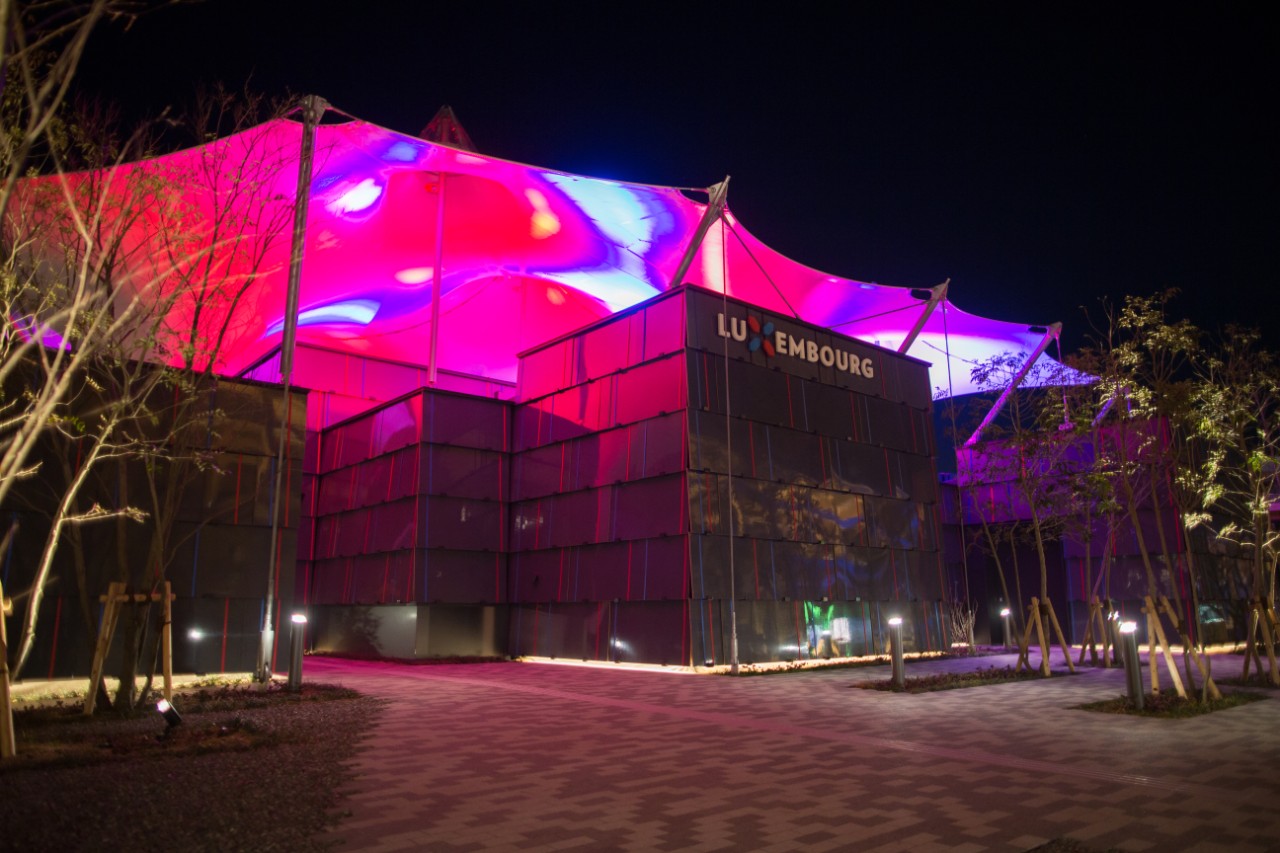 At night, the Luxembourg Pavilion with its membrane roof is illuminated in bright colours.